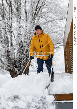 man in winter clothes with snow shovel cleaning snow from the terrace of the building 123074036