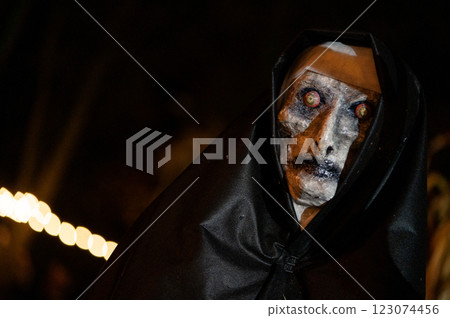 Scary Halloween witch with red eyes in a black cloak in a gloomy environment Scary Halloween witch with red eyes in a black cloak in a gloomy environment 123074456