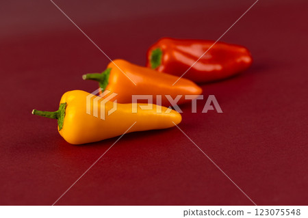 A Vibrant Display of Miniature Peppers: Yellow, Orange, and Red Varieties on a Deep Red Background A Vibrant Display of Miniature Peppers: Yellow, Orange, and Red Varieties on a Deep Red Background 123075548