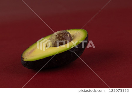 Vibrant Avocado Halves Displaying Rich Green Flesh and Shiny Brown Pit on a Burgundy Background Perfect for Culinary Inspiration and Healthy Eating Enthusiasts Vibrant Avocado Halves Displaying Rich Green Flesh and Shiny Brown Pit on a Burgundy Background Perfect for Culinary Inspiration and Healthy Eating Enthusiasts 123075553