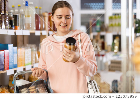 Girl customer in supermarket examines jar of lentil, chooses food-stuff in grocery Girl customer in supermarket examines jar of lentil, chooses food-stuff in grocery 123075959