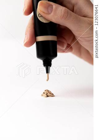 A close-up of a hand holding a foundation tube above a small dollop of cream, demonstrating the application of makeup in a minimalistic and artistic way that highlights beauty products. A close-up of a hand holding a foundation tube above a small dollop of cream, demonstrating the application of makeup in a minimalistic and artistic way that highlights beauty products. 123076641