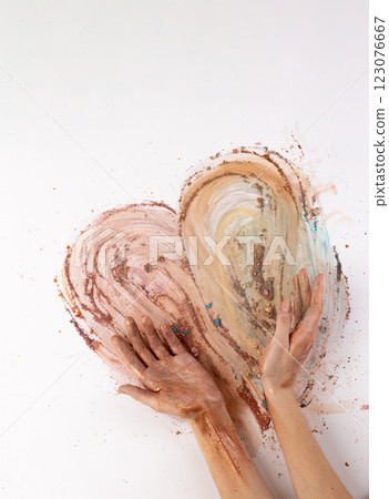 Artistic Exploration: Hands Creating a Heart with Various Earthy Tones of Pigments Spread on a White Background Symbolizing Love and Creativity in Art Expression 123076667