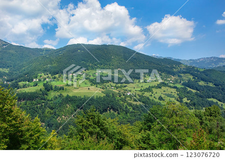 Lush green hills embrace a serene valley under a bright blue sky in Italy 123076720