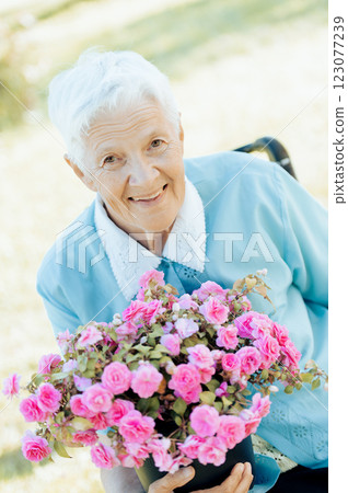 Portrait of smiling senior woman holding a purple flower pot outdoors 123077239