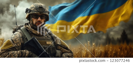 Soldier in full combat gear standing in wheat field with Ukrainian flag waving behind, displaying resilience, readiness, and pride in national service. 123077246