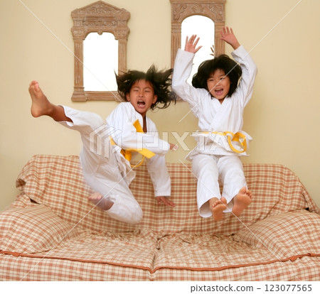 Two little asian judo gils jump on sofa 123077565