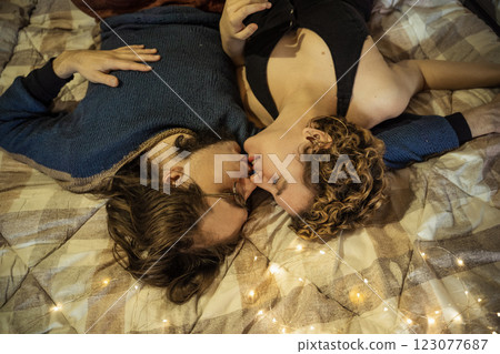 Couple sharing a loving kiss while lying on a cozy bed adorned with soft lighting during a quiet evening 123077687