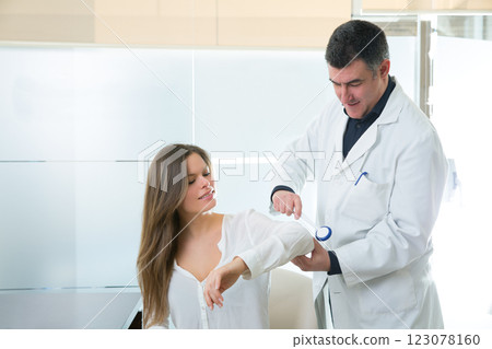 Doctor checking elbow with reflex round hammer to woman 123078160