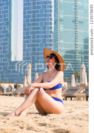 A Stylish Woman in a Blue Swimsuit, Hat, and Sunglasses Exudes Confidence and Elegance While Relaxing on an Urban Beach, Enjoying the Sun and Vibrant Atmosphere of City Life, Perfectly Capturing the A Stylish Woman in a Blue Swimsuit, Hat, and Sunglasses Exudes Confidence and Elegance While Relaxing on an Urban Beach, Enjoying the Sun and Vibrant Atmosphere of City Life, Perfectly Capturing the 123078695