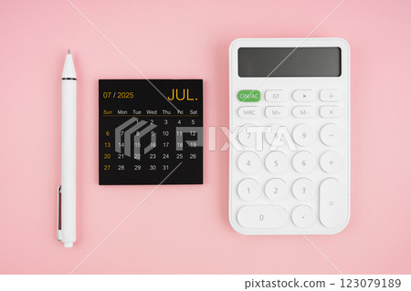 July 2025 calendar and white calculator with pen on pink background. July 2025 calendar and white calculator with pen on pink background. 123079189