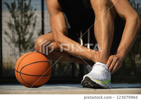 Basketball ankle injury or pain. Basketball player check legs after workout of sport stadium. Professional athlete or sportsman with accident. Man check pain in leg after sport workout. Close up. 123079968