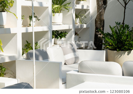 Bright and inviting outdoor lounge features sleek white furniture complemented by vibrant greenery. Sunlight casts soft shadows, creating a serene atmosphere perfect for relaxation. Bright and inviting outdoor lounge features sleek white furniture complemented by vibrant greenery. Sunlight casts soft shadows, creating a serene atmosphere perfect for relaxation. 123080106