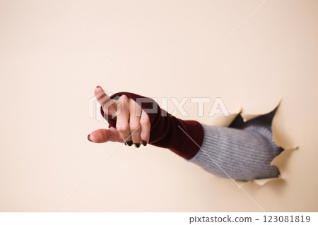 A woman's hand in a knitted burgundy mitten shows a gesture her index finger 123081819