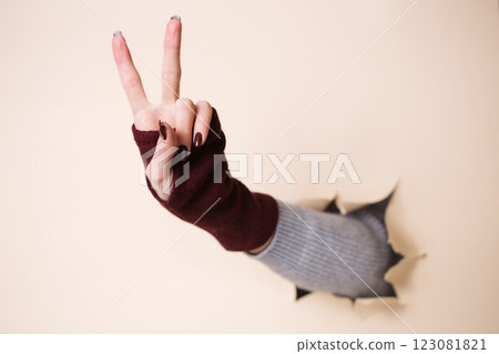 A woman's hand in a knitted burgundy mitten shows a gesture of victory hand A woman's hand in a knitted burgundy mitten shows a gesture of victory hand 123081821