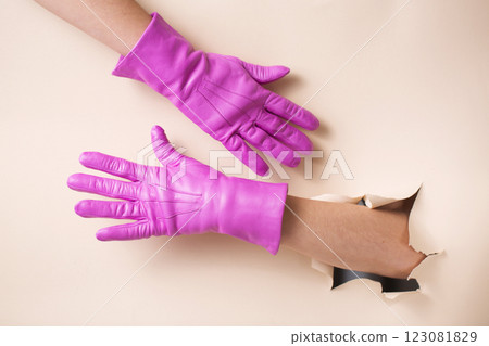 Two female hands in bright warm leather gloves on a background of beige paper with a hole. Two female hands in bright warm leather gloves on a background of beige paper with a hole. 123081829