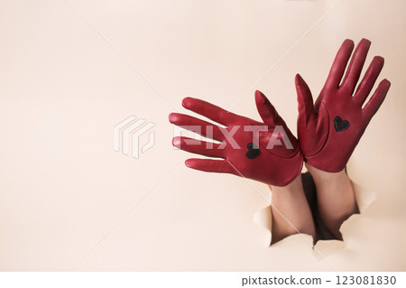 Two female hands in burgundy leather gloves with a heart inserted into a hole in beige paper Two female hands in burgundy leather gloves with a heart inserted into a hole in beige paper 123081830
