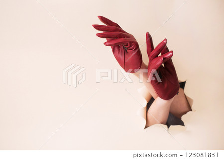 Two female hands in burgundy leather gloves inserted into a hole in paper Two female hands in burgundy leather gloves inserted into a hole in paper 123081831