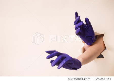 Two female hands in blue leather gloves trying to crawl through a hole in beige paper Two female hands in blue leather gloves trying to crawl through a hole in beige paper 123081834