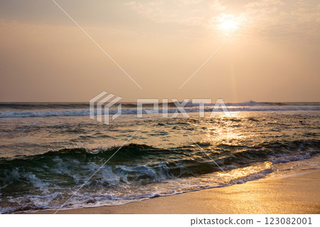 The ocean is calm and the sun is setting, surfers with boards are riding the waves The ocean is calm and the sun is setting, surfers with boards are riding the waves 123082001
