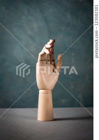 A wooden hand with red nail polish on it is standing on a grey surface 123082381