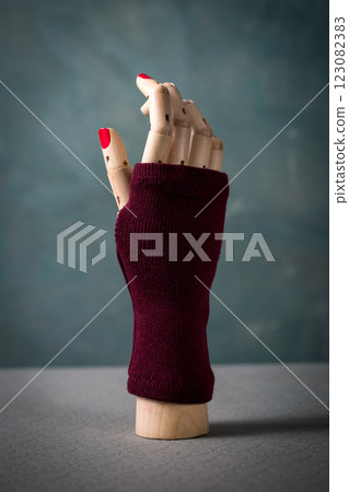 A mannequin hand with red nails and a maroon mitten 123082383