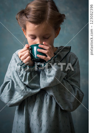 A young girl is drinking from a green cup. She is wearing a vintage dress A young girl is drinking from a green cup. She is wearing a vintage dress 123082396