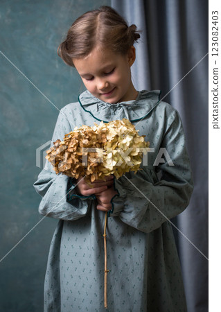 A girl is holding a branch with a hydrangea flower. She is wearing a green vintage dress A girl is holding a branch with a hydrangea flower. She is wearing a green vintage dress 123082403