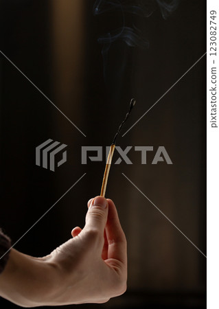 A hand holds an extinguished match on a dark background 123082749