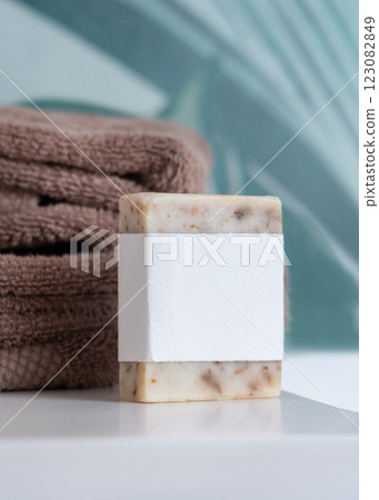 Beige soap with blank label near brown folded towels on basin in tropical bathroom close up, mockup 123082849
