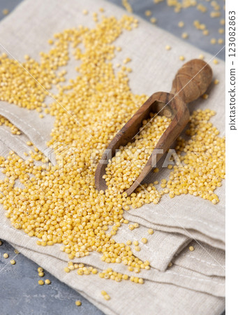 Raw uncooked yellow millet grain in a wooden scoop on grey table, top view. Ancient food 123082863