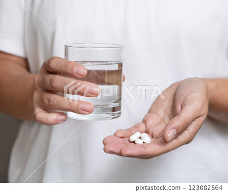 Woman in white t-shirt holding white pills in cupped hand and water glass in hand closeup 123082864