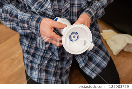 An elderly man focuses on assembling plumbing components for the kitchen and bathroom on a wooden floor. 123083759