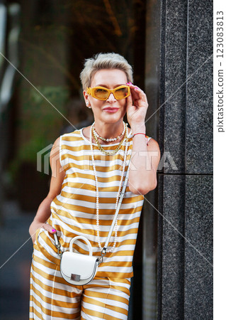 Portrait Beautiful Mature Woman with Short Hair, pearl necklace and yellow Sunglasses in stylish clothes Striped sleeveless top at Summer Outdoors in City, Confidence, fashion and Style 123083813