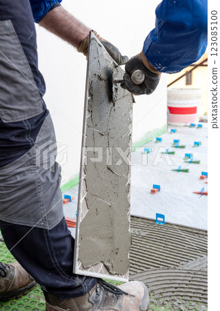 Tiler at work installing new floor with tiles. Construction. 123085100