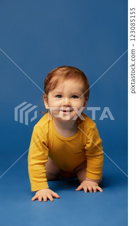 Portrait of happy little baby crawling forward with joyful expression, wearing casual yellow outfit against deep blue background. 123085155