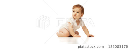 Banner. Baby in onesie, sitting with one hand on floor and head turned to side against white background with negative space to insert text. 123085176