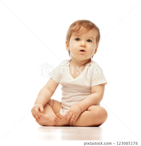 Portrait of of little, curious baby, dressed white onesie, sitting and gazing upward with wide eyes and relaxed posture against white background. 123085178