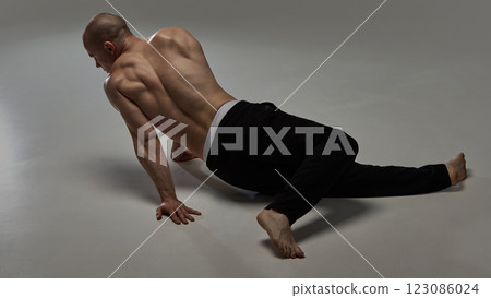 Rear view of shirtless male model moving on floor with sculpted back and elegant posture against minimalist backdrop. 123086024
