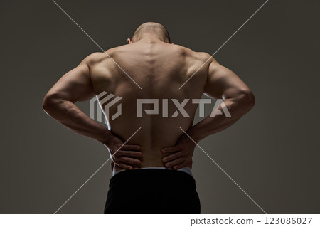 Close-up of male model's muscular, healthy back with hands resting on waist against dramatic lighting. Concept of natural beauty. 123086027