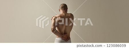Banner. Masculine man, dressed underwear, standing with back arched and arms crossed in emotional movement against soft- beige studio background. Banner. Masculine man, dressed underwear, standing with back arched and arms crossed in emotional movement against soft- beige studio background. 123086039