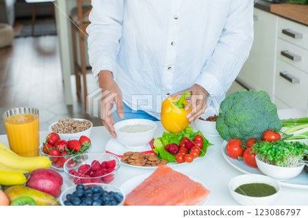Female Nutritionist expert makes healthy balanced diet plate according to proportions of nutrients. Plate with pie chart of fruit, vegetables, grains, proteins on kitchen table with ingredients. 123086797