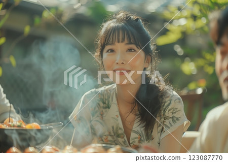 A joyful woman enjoying an outdoor barbecue, surrounded by friends and nature. 123087770