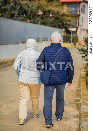 Elderly couple walking together on a quiet street in warm jackets. Romantic moment of senior couple in an urban setting. Autumn, happy family, aged people concept 123089194