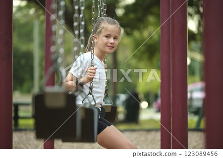 Young pretty smiling teenage girl playing alone on swings on summer playground Young pretty smiling teenage girl playing alone on swings on summer playground 123089456