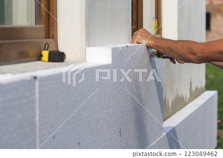 Worker hand with level and knife measuring and cutting white rigid polyurethane foam sheet on wall at newly installed plastic window. Modern technology, renovation, insulation concept. 123089462