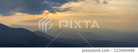 Wide panorama, fantastic view of covered with morning mist green Carpathian mountains at dawn under dark clouds and light pink sky before sunrise. Beauty of nature, tourism and traveling concept. 123089486
