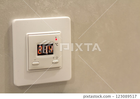 White electronic programmable digital thermostat on light wall copy space background. Climate control, comfortable home temperature, energy saving concept. 123089517