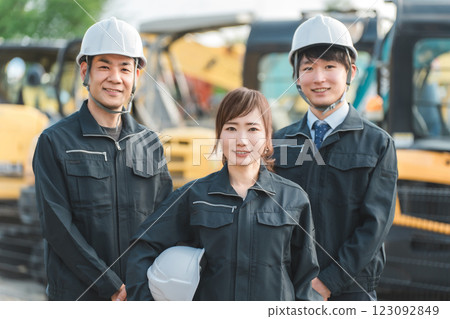 Male and female construction and building workers in work clothes in front of heavy machinery Male and female construction and building workers in work clothes in front of heavy machinery 123092849