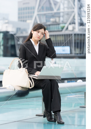 A young businesswoman worries while working on a laptop outdoors at OASIS21 Water Spaceship, Sakae, Nagoya A young businesswoman worries while working on a laptop outdoors at OASIS21 Water Spaceship, Sakae, Nagoya 123093284